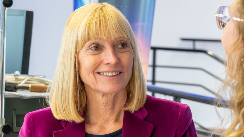 Eine Frau in einem pinken Blazer lächelt und unterhält sich mit einer anderen Person.