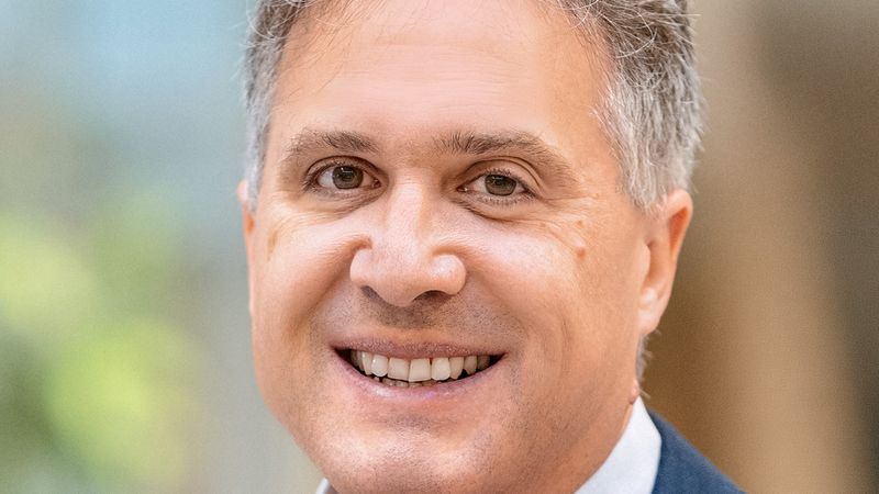 Ein Porträt eines lächelnden Mannes in einem blauen Anzug und einem hellblauen Hemd.