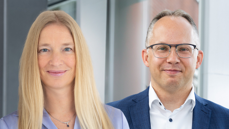 Ein Porträt von zwei Personen, einer Frau und einem Mann, die nebeneinander stehen und in die Kamera lächeln.