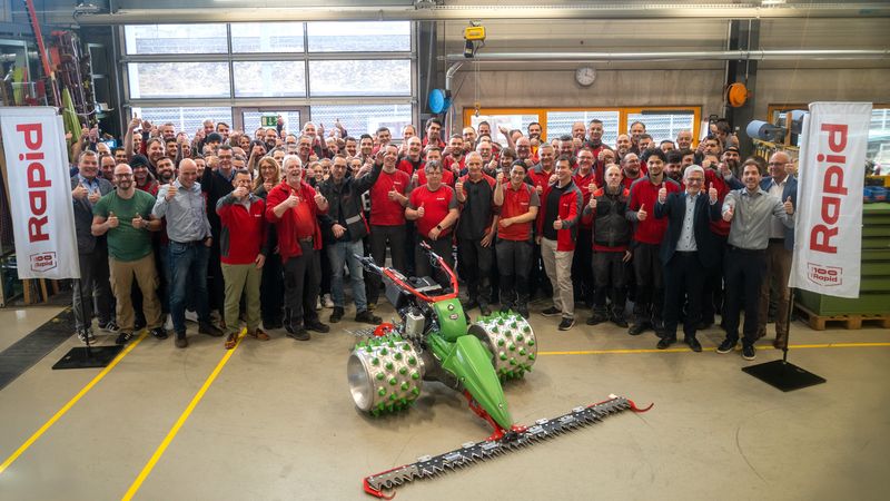 Eine große Gruppe von Menschen posiert in einer Werkhalle um eine grüne Maschine herum.