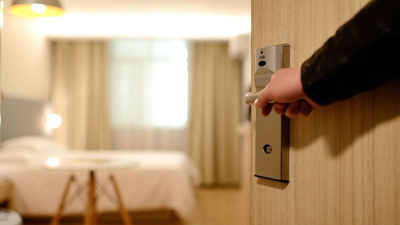 Eine Person öffnet die Tür zu einem gemütlichen Hotelzimmer mit einem großen Bett und warmem Licht.