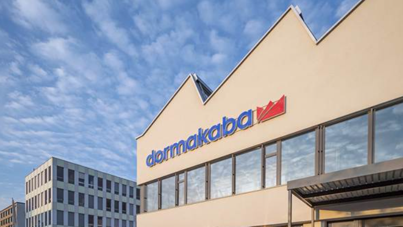 Ein modernes Gebäude mit dem dormakaba-Logo auf der Fassade unter einem blauen Himmel.