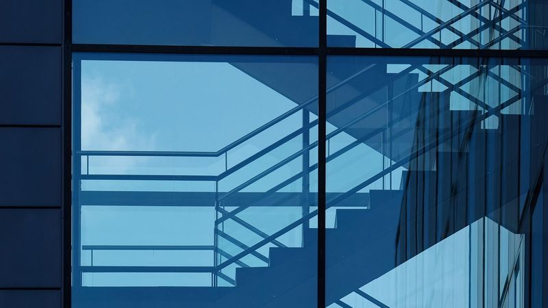 Ein modernes Treppenhaus mit Glasfassade, das sich in einem Gebäude spiegelt.