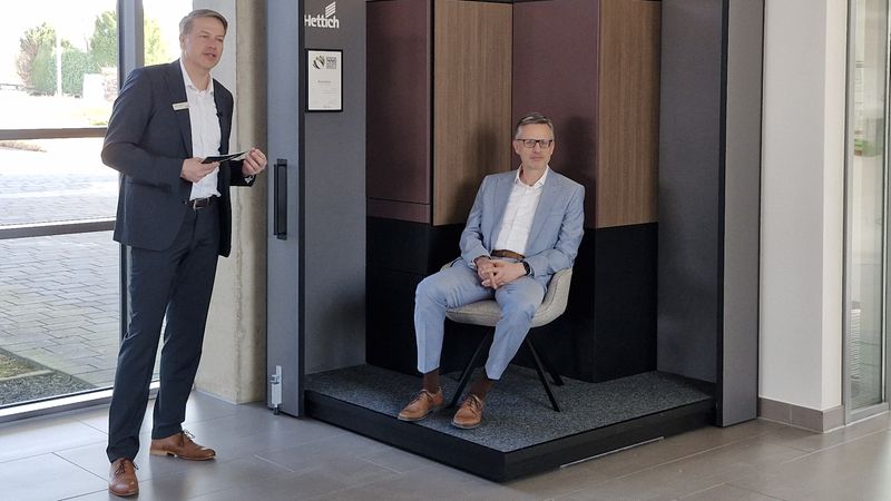 Zwei Männer präsentieren moderne Büromöbel in einem Ausstellungsraum.