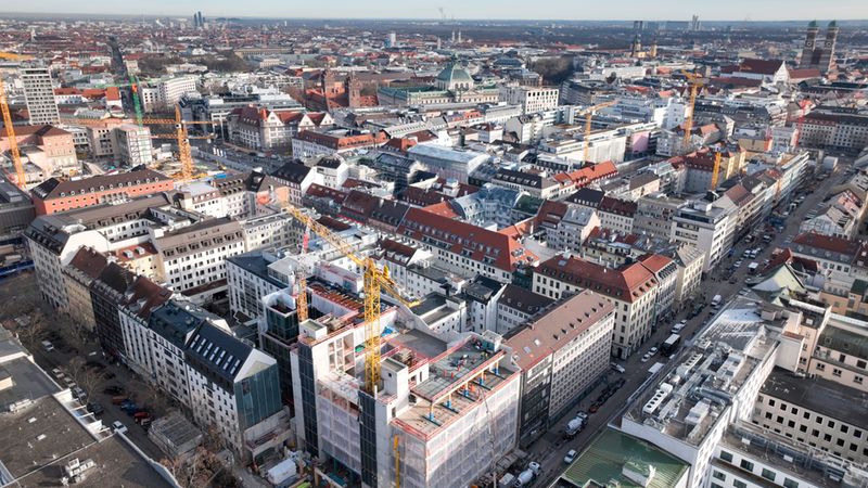 Luftaufnahme von München mit einem Baukran im Vordergrund, der über den Dächern der Stadt ragt.
