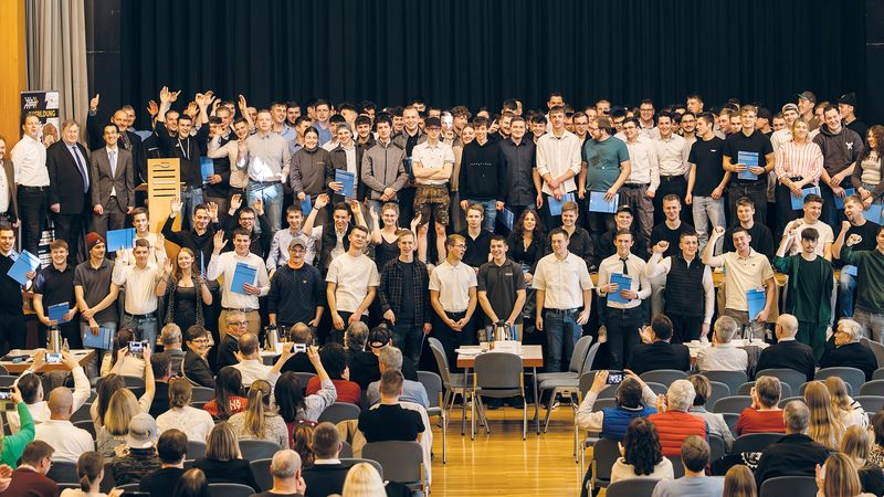 Ein Gruppenfoto einer Abschlussfeier mit vielen jungen Erwachsenen auf einer Bühne, die ihre Zertifikate präsentieren.