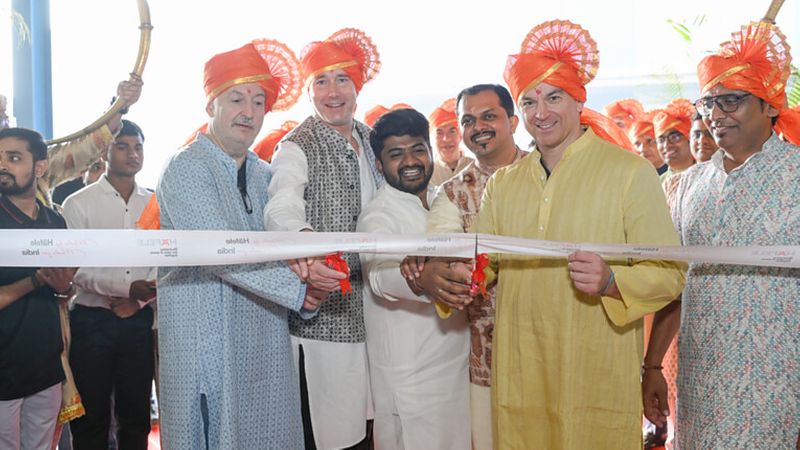 Eine Gruppe von Menschen in traditioneller Kleidung und orangefarbenen Turbanen schneidet ein Band bei einer feierlichen Eröffnung durch.