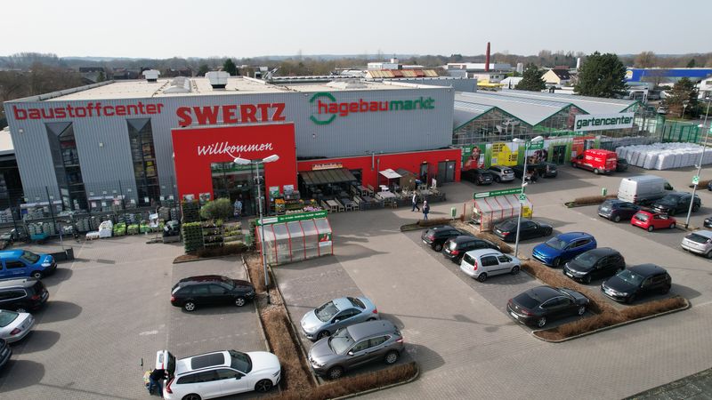 Außenansicht eines Hagebaumarkts mit Parkplatz und mehreren Autos.