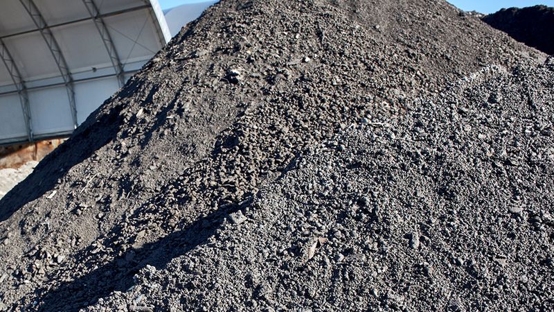 Ein großer Haufen Asche auf einem Industriegelände, der in der Sonne liegt.