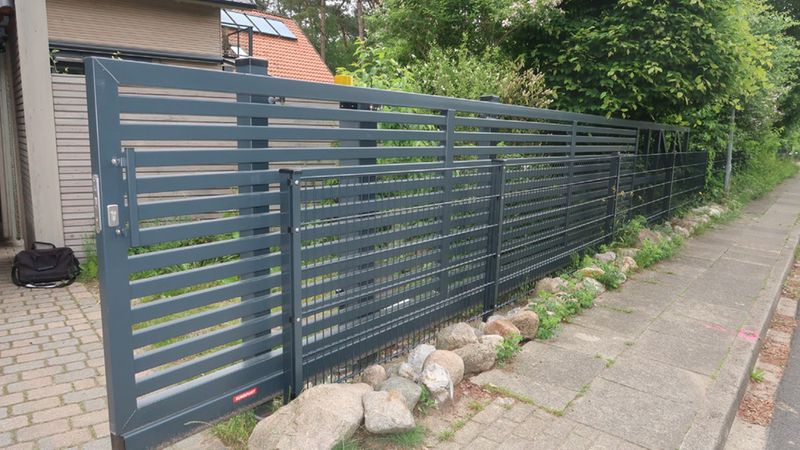 Ein modernes Metalltor mit horizontalen Streben, das einen gepflegten Garten von der Straße trennt.