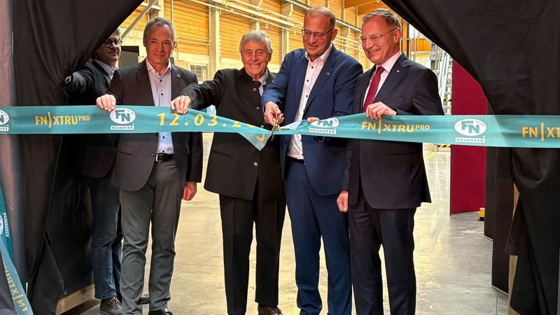 Vier Männer bei der feierlichen Eröffnung eines neuen Gebäudes, während sie ein Band durchschneiden.