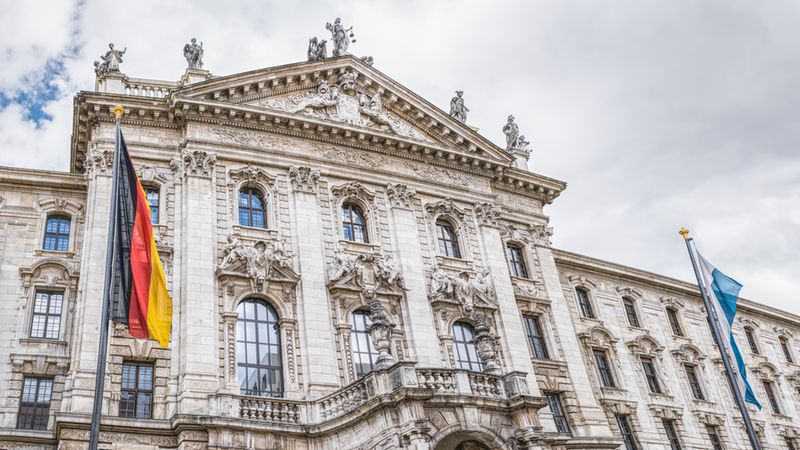 Der Justizpalast in München mit seiner beeindruckenden neobarocken Fassade und den deutschen sowie bayerischen Flaggen im Vordergrund.