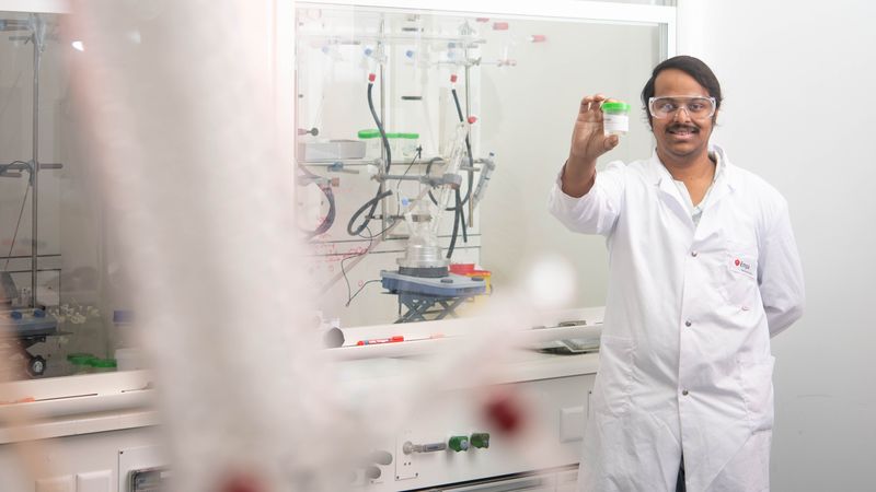 Ein Wissenschaftler im weißen Laborkittel hält ein kleines Glasgefäß in einem Labor.