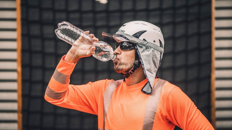 Ein Bauarbeiter in Schutzkleidung trinkt Wasser aus einer Flasche.