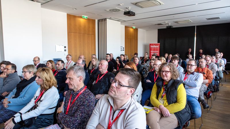 Eine Gruppe von Menschen sitzt aufmerksam in einem Konferenzraum und hört einem Vortrag zu.