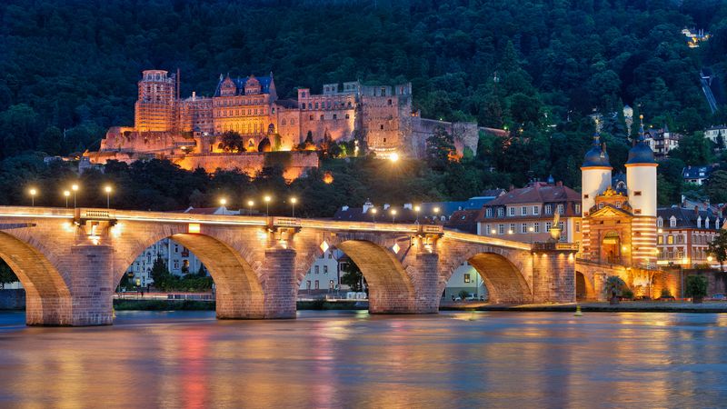 Das Bild zeigt das beleuchtete Heidelberger Schloss und die Alte Brücke bei Nacht, die sich majestätisch über den Neckar erstreckt.