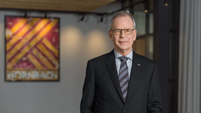 Ein Geschäftsmann im Anzug steht in einem modernen Büro mit einem Gemälde im Hintergrund.