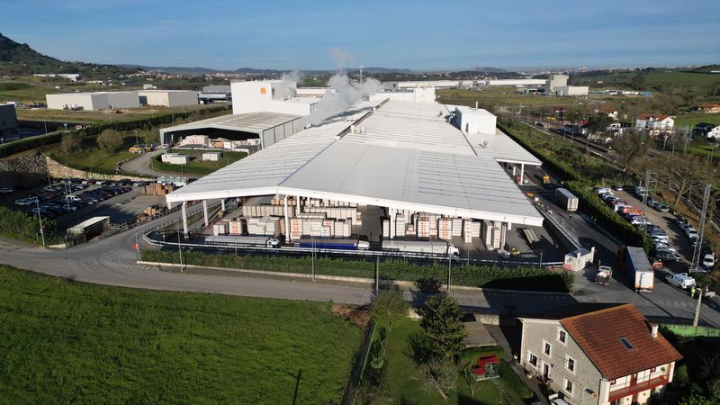 Luftaufnahme einer großen Industrieanlage mit mehreren Gebäuden und Lagerflächen, umgeben von ländlicher Landschaft.