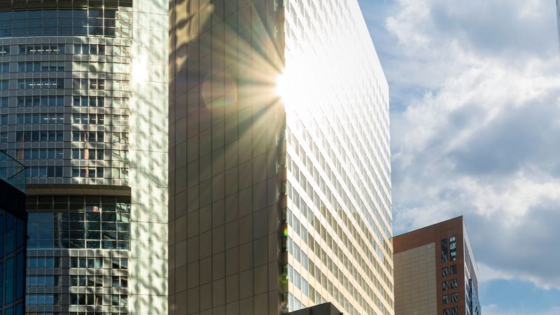 Ein modernes Hochhaus in Frankfurt mit Sonnenstrahlen, die sich auf der Glasfassade spiegeln.