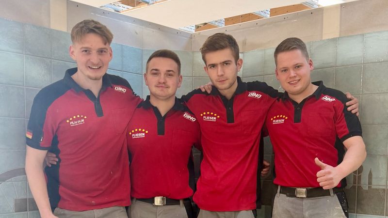 Ein Team von vier Handwerkern in roten Arbeitshemden steht vor einer gefliesten Wand.