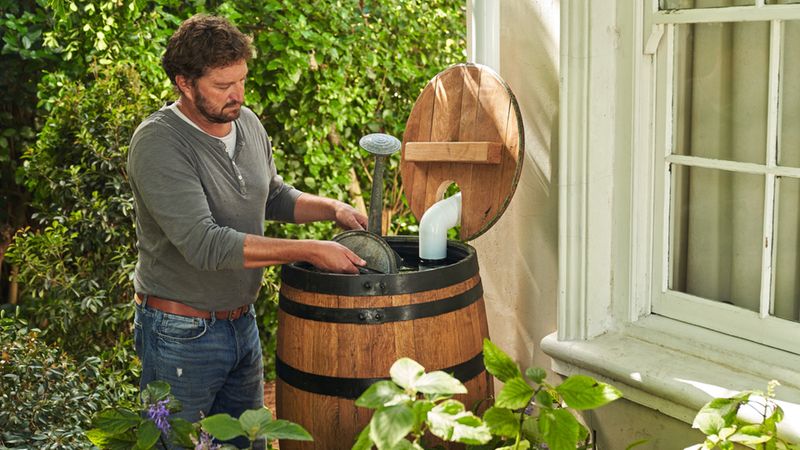 Ein Mann steht im Garten neben einem Regenfass und überprüft den Wasserstand.