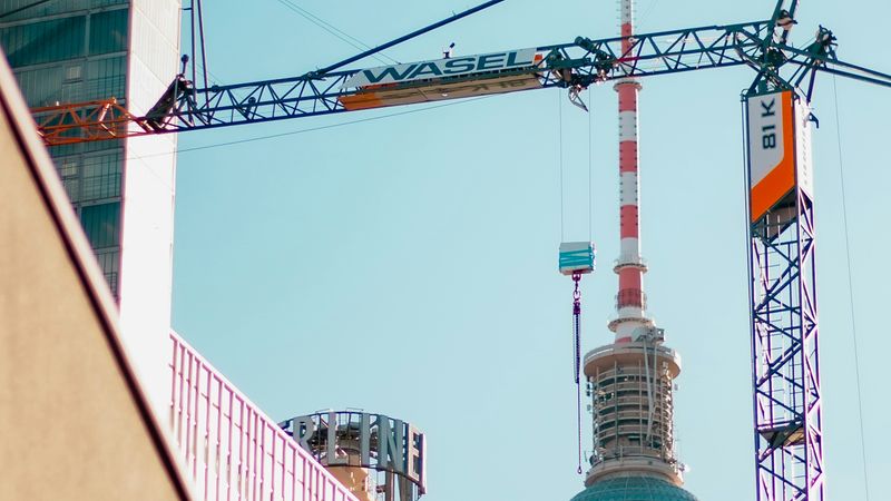 Der Berliner Fernsehturm hinter einem Baukran und modernen Gebäuden bei klarem Himmel.
