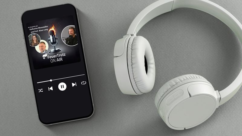 Ein Smartphone mit einer Podcast-App auf dem Bildschirm, daneben weiße Kopfhörer auf einer grauen Oberfläche.