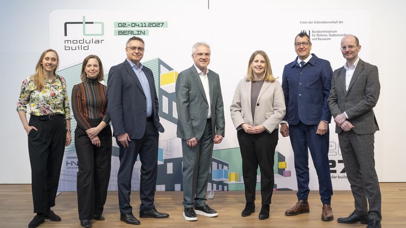 Gruppenfoto von sieben Personen vor einem Konferenzbanner in Berlin.