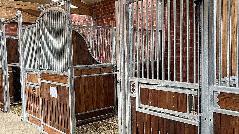 Ein moderner Pferdestall mit mehreren Boxen aus Holz und Metall, die in einer Reihe angeordnet sind.