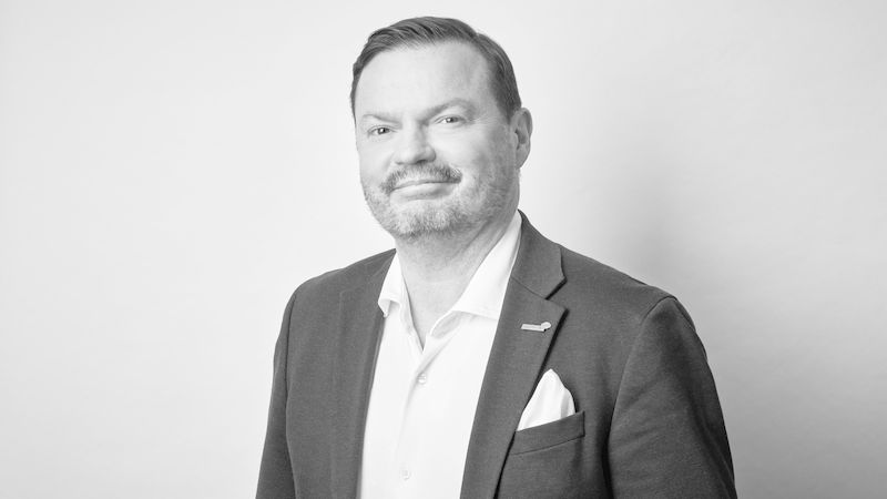 Ein schwarz-weiß Porträt eines Mannes in einem Anzug vor einem neutralen Hintergrund.