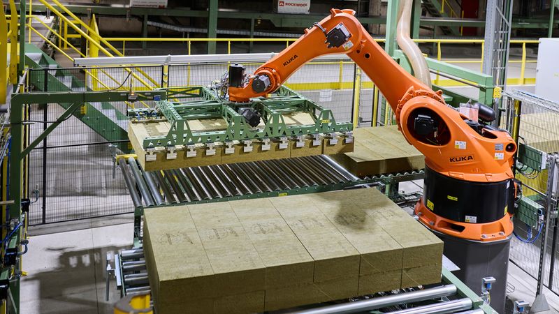 Ein Industrieroboter in einer Fabrik, der große Isolierplatten auf einem Förderband bewegt.