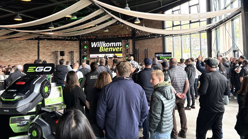 Eine Veranstaltung in einer Halle mit vielen Menschen, die einer Präsentation folgen. Im Vordergrund sind Produkte der Marke EGO zu sehen.