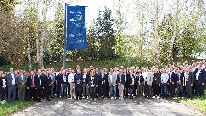 Ein Gruppenfoto von Menschen, die vor einer Fahne im Freien stehen.