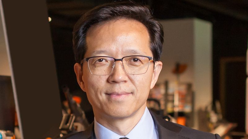 Ein Mann in einem Anzug steht in einem Innenraum und schaut in die Kamera.