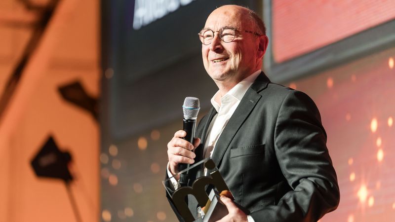 Rolf Buch im Anzug hält ein Mikrofon und den immobilienmanager-Award in der Hand, während er auf einer Bühne steht.