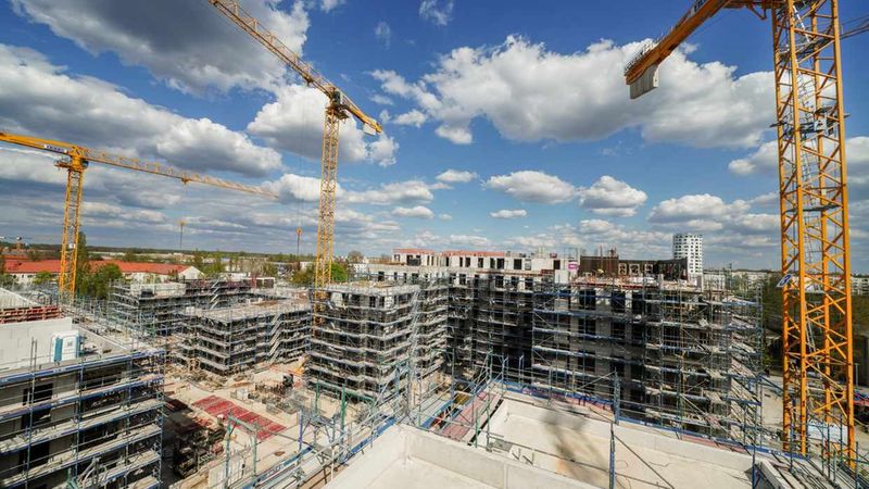 Eine große Baustelle mit mehreren Baukränen und im Bau befindlichen Hochhäusern unter einem blauen Himmel mit Wolken.