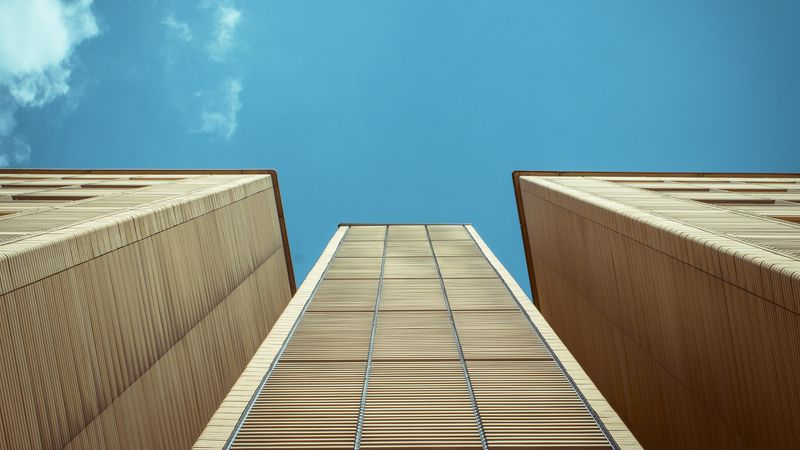 Ein modernes Hochhaus mit einer Fassade aus Holz, das in den blauen Himmel ragt.