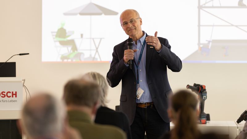 Ein Mann hält einen Vortrag auf einer Konferenz und spricht in ein Mikrofon.