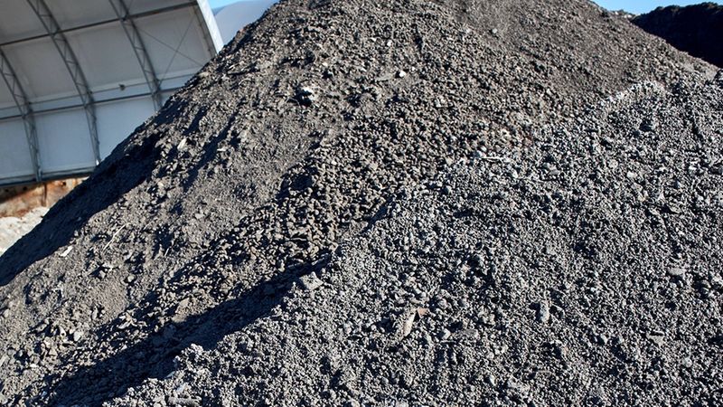 Ein großer Haufen Hausmüllverbrennungsasche auf einem Industriegelände unter freiem Himmel.