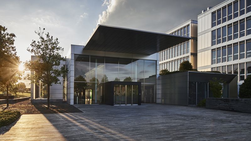 Ein modernes Bürogebäude mit Glasfassade und klaren Linien, umgeben von Bäumen bei Sonnenuntergang.