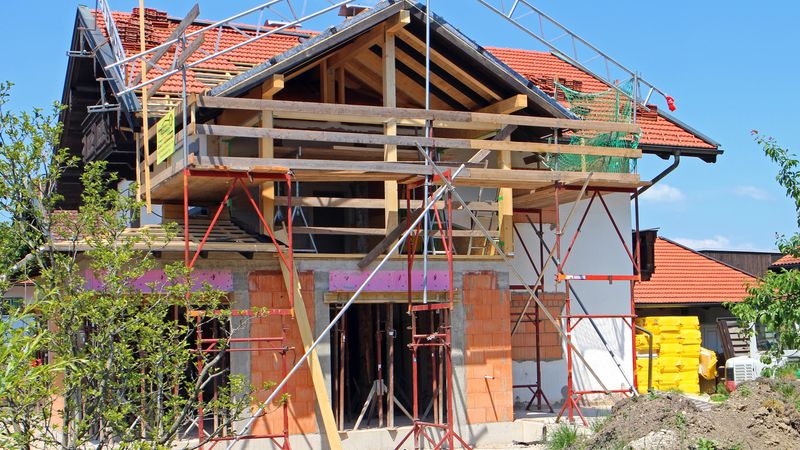 Ein im Bau befindliches Haus mit Gerüst und roten Ziegeln auf dem Dach.