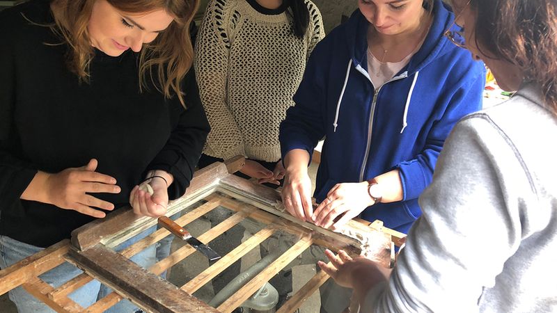 Eine Gruppe von Menschen restauriert gemeinsam ein altes Fenster.