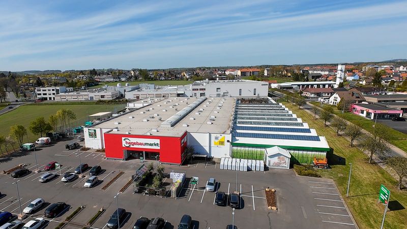 Luftaufnahme eines Baumarkts mit großem Parkplatz und Solarpaneelen auf dem Dach.