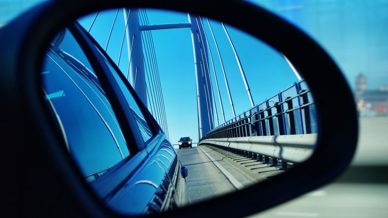 Ein Auto fährt über eine Brücke, gesehen im Rückspiegel eines anderen Fahrzeugs.