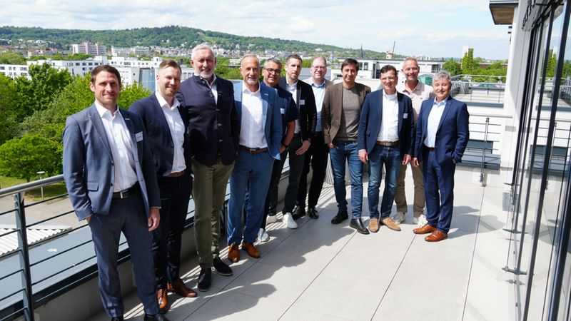 Eine Gruppe von Geschäftsleuten steht auf einer Dachterrasse mit Blick auf die Stadt im Hintergrund.