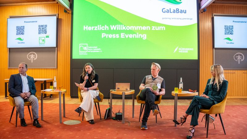 Eine Pressekonferenz der GaLaBau mit vier Personen auf einer Bühne, die vor einem großen Bildschirm sitzen.
