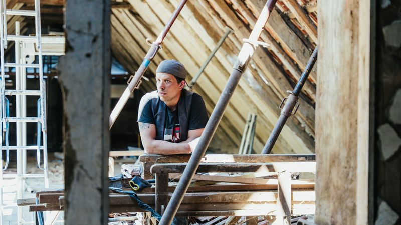 Ein Handwerker lehnt auf einem Gerüst in einem Dachboden während Renovierungsarbeiten.