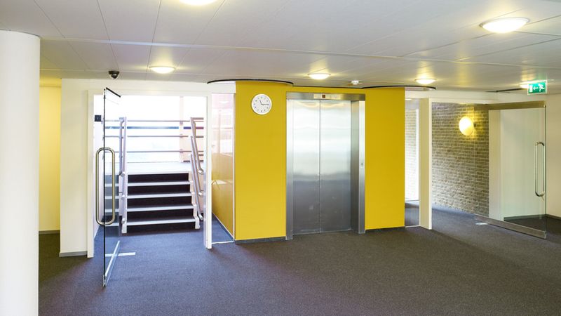 Eine moderne Büro-Lobby mit einem Aufzug in der Mitte und gelben Wänden.