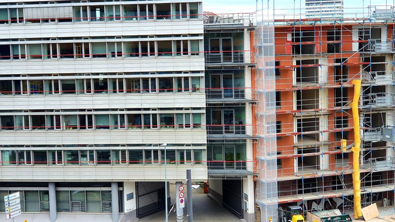 Ein modernes Bürogebäude neben einer Baustelle mit Gerüsten und Baukränen.