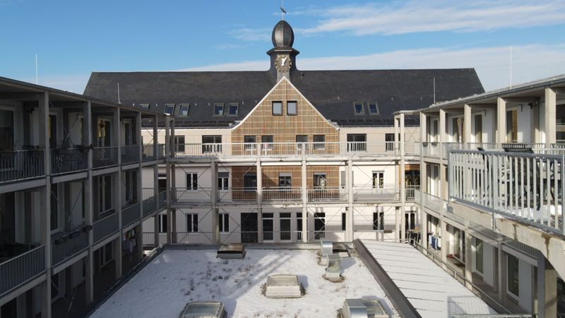 Ein Innenhof mit schneebedecktem Boden und einem zentralen Gebäude mit markantem Dach.